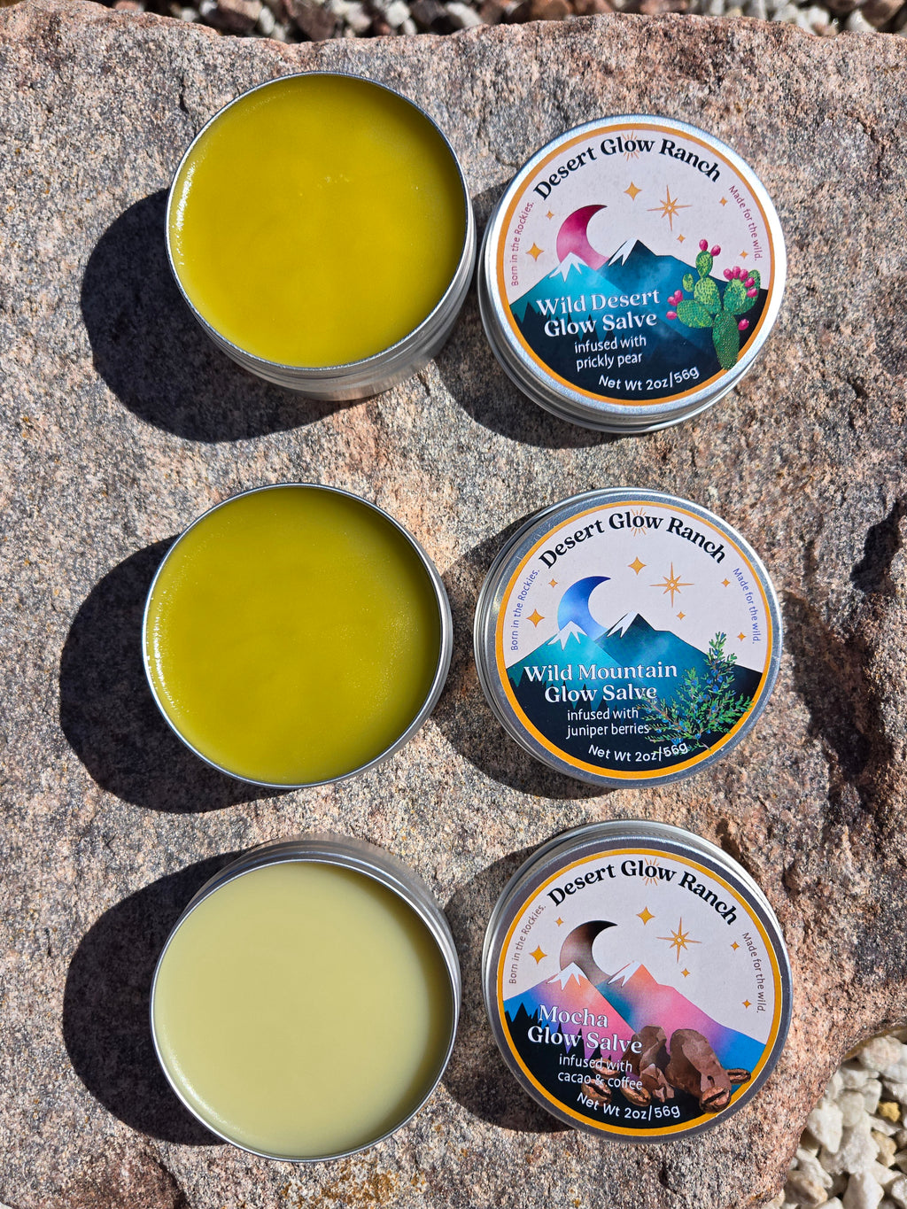 Flat lay of Wild Desert Glow, Wild Mountain Glow, and Mocha Glow Salve tins open and closed on a stone surface