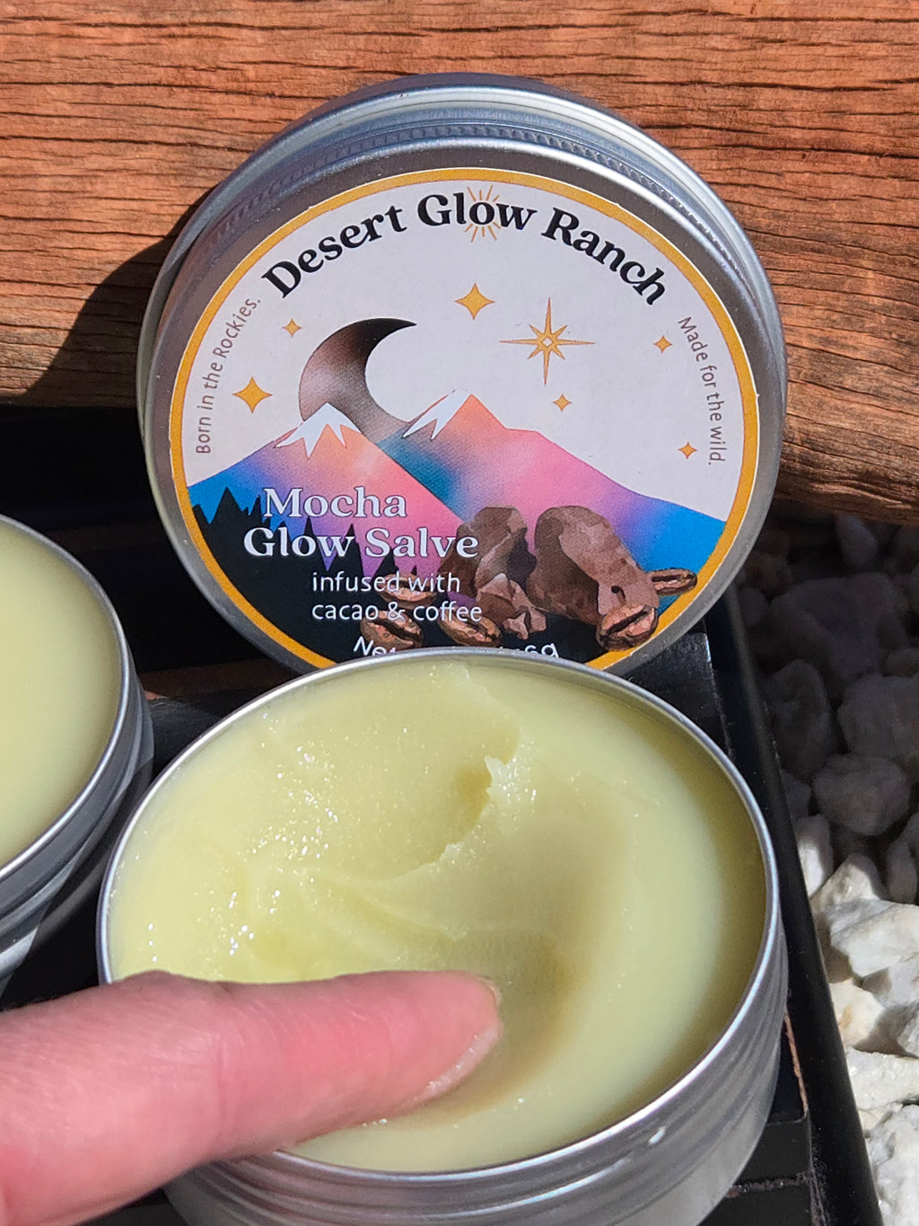 Close-up of mocha glow salve organic coffee and chocolate moisturizer with finger showing smooth texture in tin