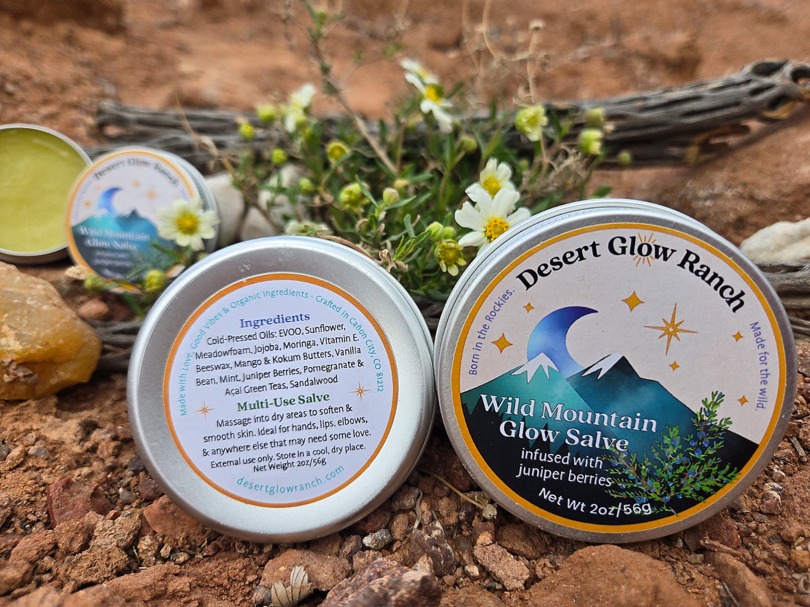 Wild Mountain Glow Salve tins with ingredients label on natural desert ground with botanicals